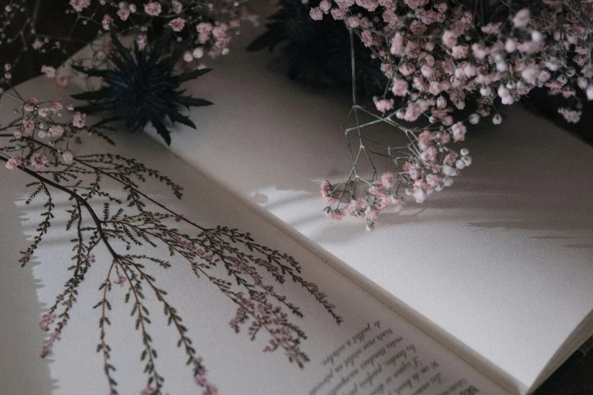 open poetry book with delicate floral illustration and pink baby’s breath flowers casting soft shadows on the pages