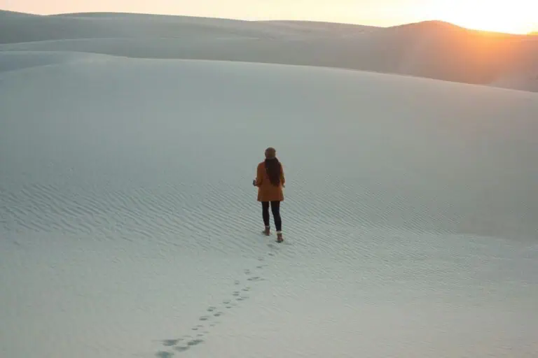 woman walking alone in the desert leaving footprints behind under a soft sunrise