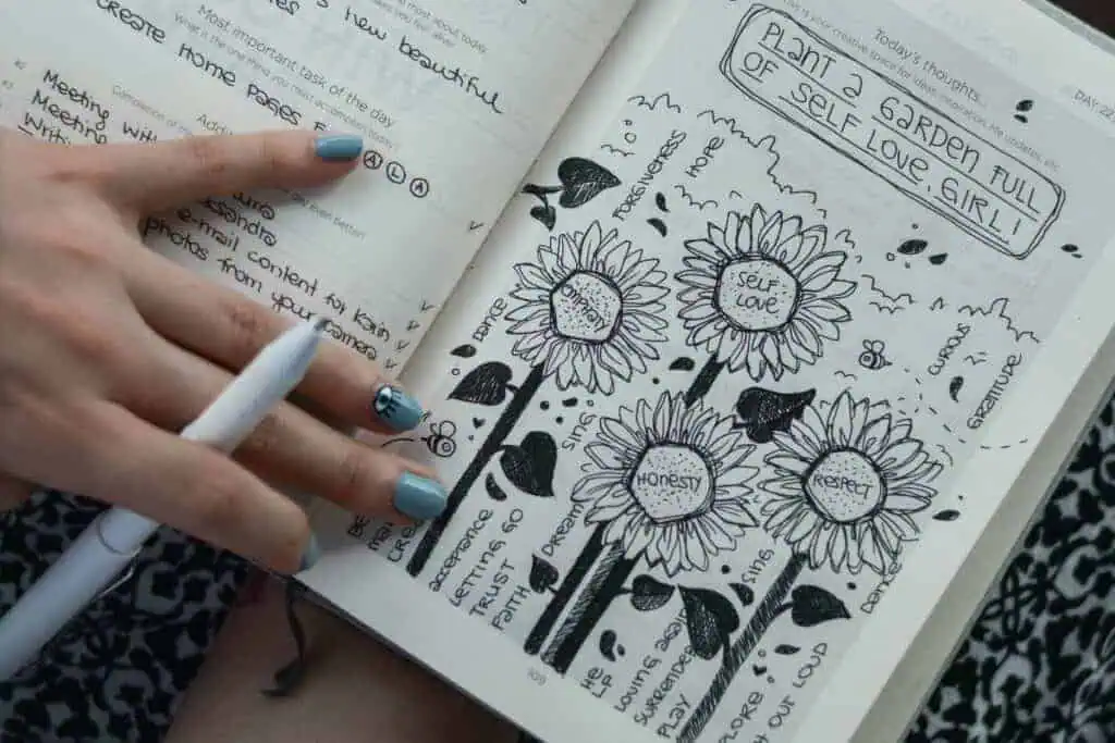 open journal with doodles and affirmations about self-love, honesty, and gratitude held by a person with painted nails