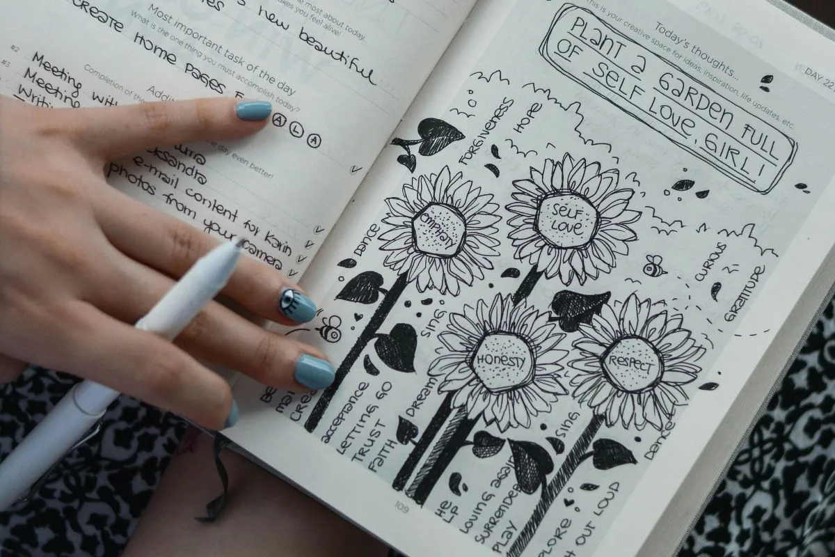 open journal with doodles and affirmations about self-love, honesty, and gratitude held by a person with painted nails