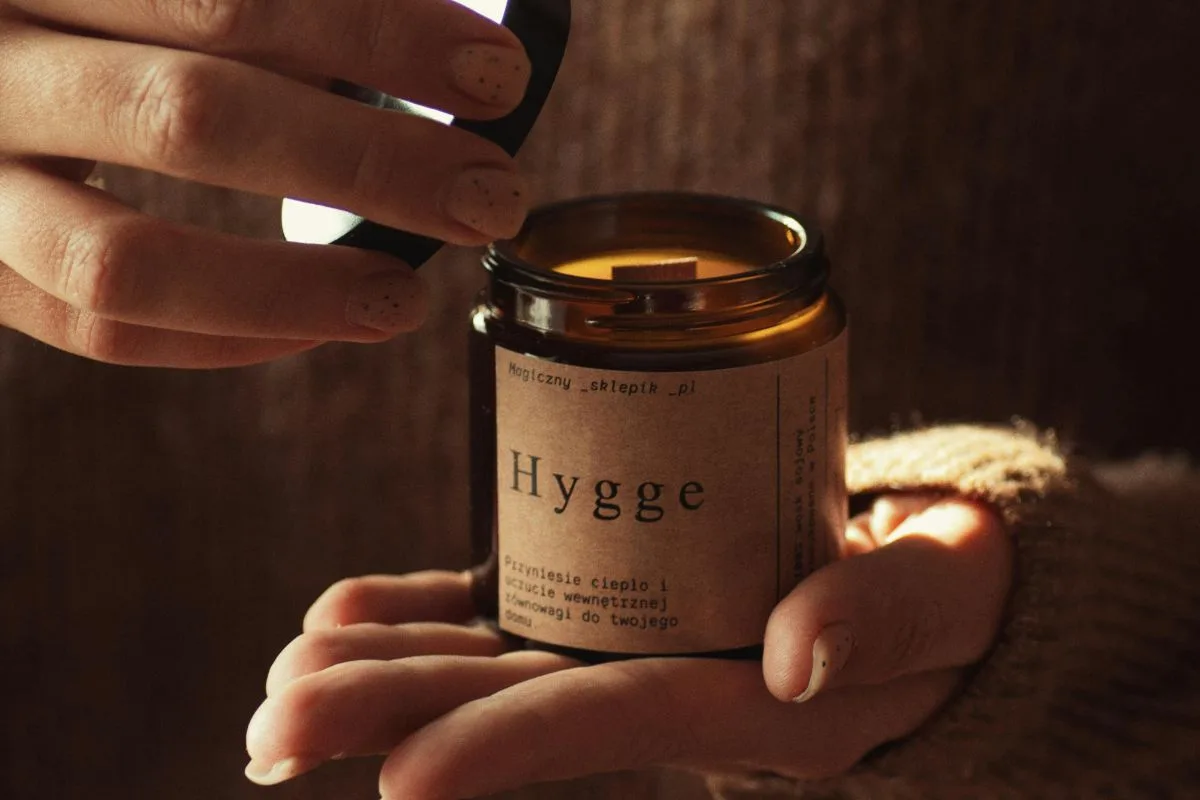 hands holding a cozy brown jar candle labeled “hygge,” capturing a warm and comforting moment in soft, golden light
