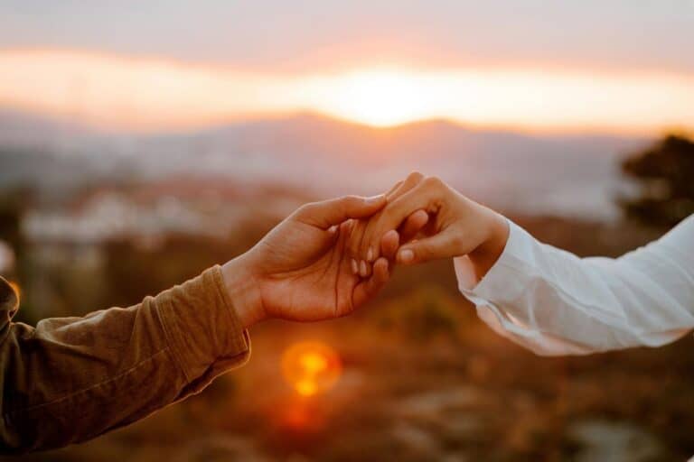 two hands reaching for each other gently with a soft golden sunset in the background