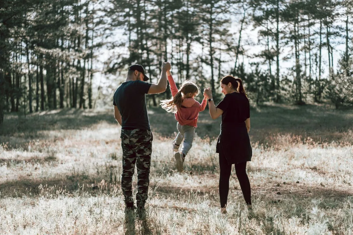 family walking hand in hand through a sunlit forest, lifting their daughter playfully