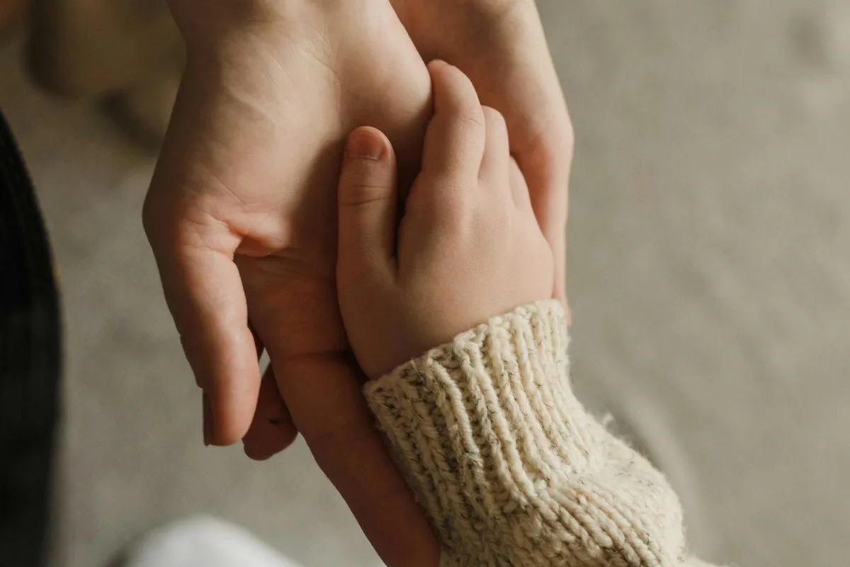 adult hand gently holding a child's hand, capturing a soft moment of love and trust