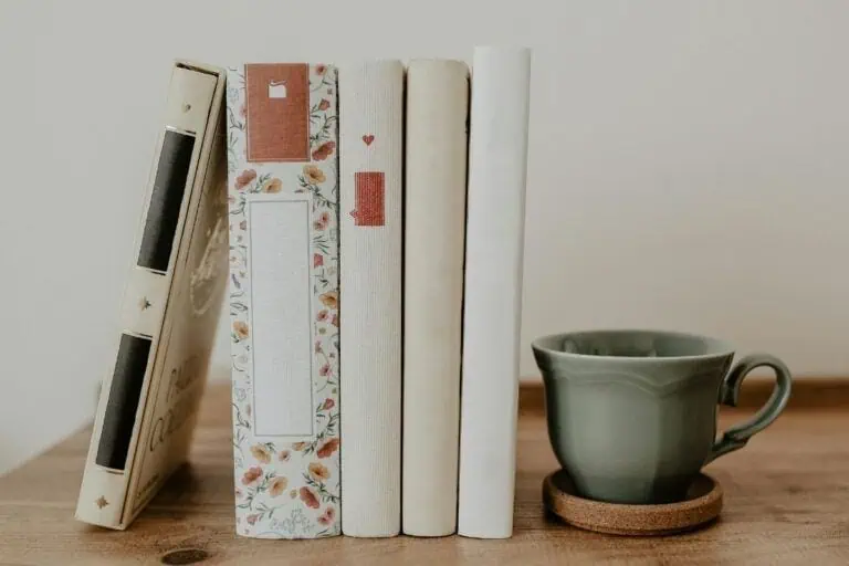 a stack of pastel-toned books with floral spines beside a green ceramic cup on a wooden table