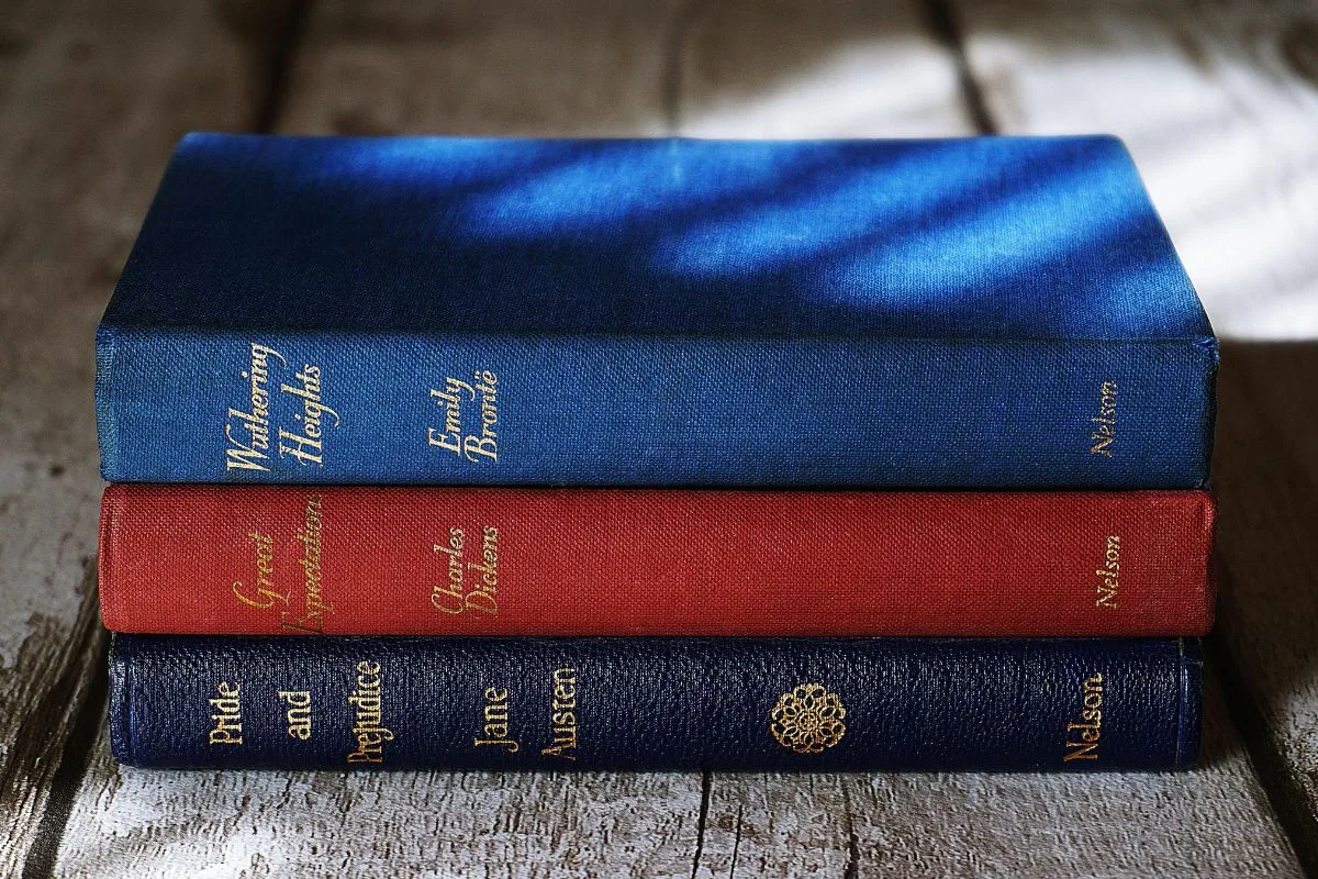 stack of classic novels with vintage covers including wuthering heights, great expectations, and pride and prejudice placed on a rustic wooden surface with soft shadow