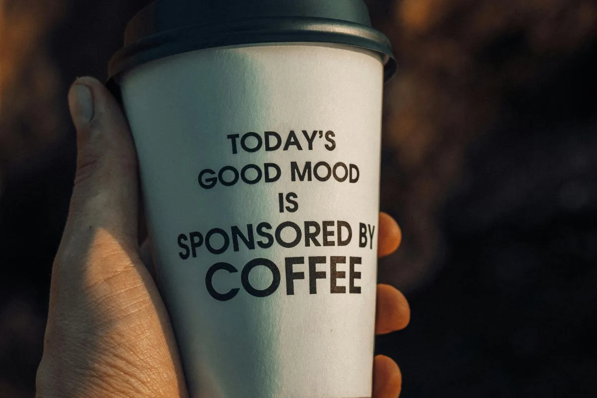 hand holding a paper coffee cup with the quote “today’s good mood is sponsored by coffee