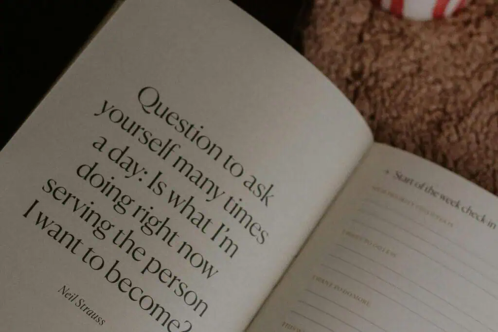 open journal with a quote by neil strauss that reads "question to ask yourself many times a day: is what I’m doing right now serving the person I want to become" placed beside a cup of tea and a green leaf
