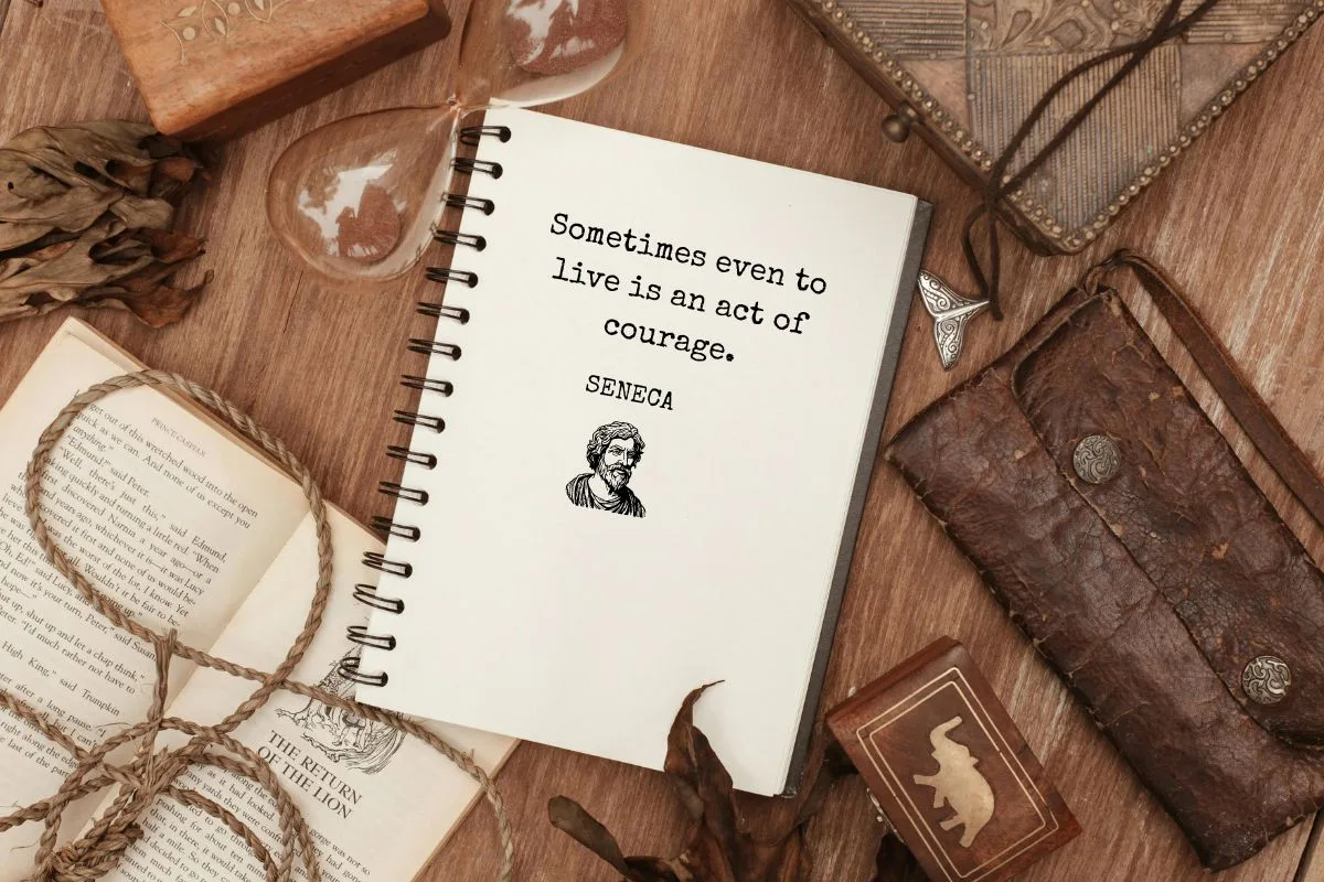 flat lay of an open vintage notebook on a wooden table with a seneca quote, surrounded by old books, leather pouch, rope, and an hourglass
