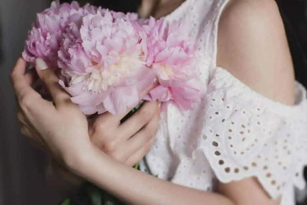 hands holding soft pink peonies in a white embroidered dress