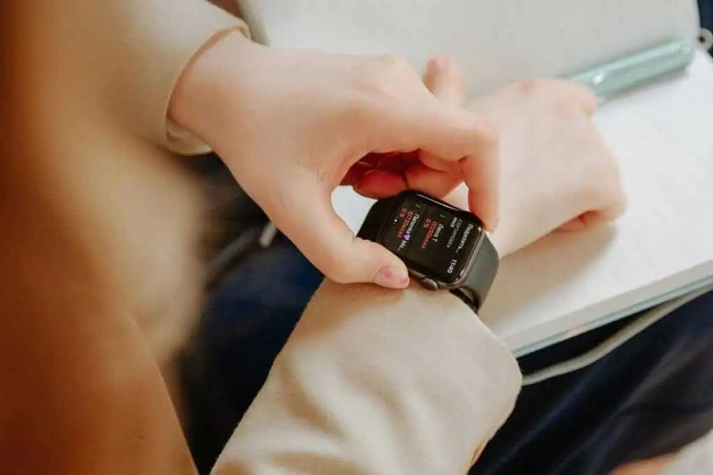a person checking time on a smartwatch while writing in a notebook