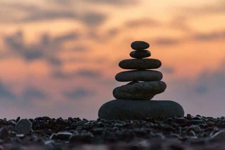 a stack of smooth stones balanced on a beach with a soft orange sunset sky in the background, symbolizing peace and mindfulness and wisdom
