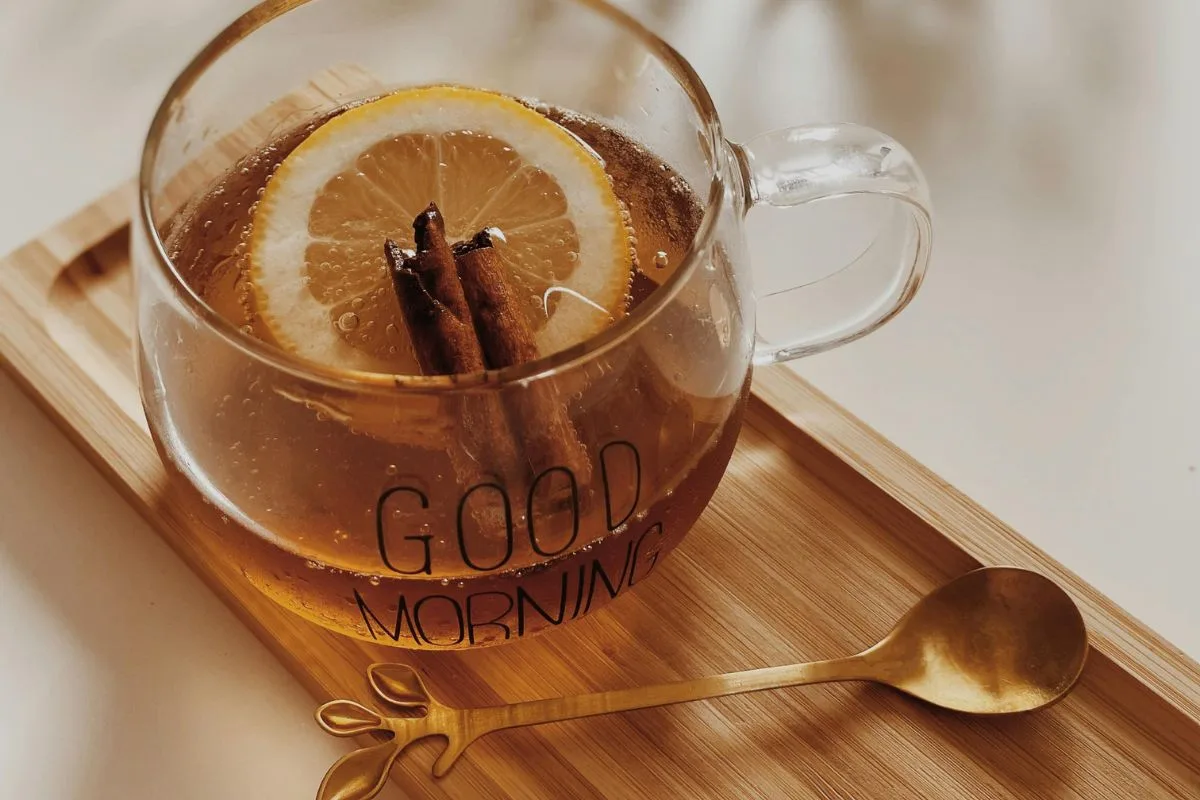 glass cup with 'good morning' text filled with lemon cinnamon tea on a wooden tray with a golden spoon placed beside it