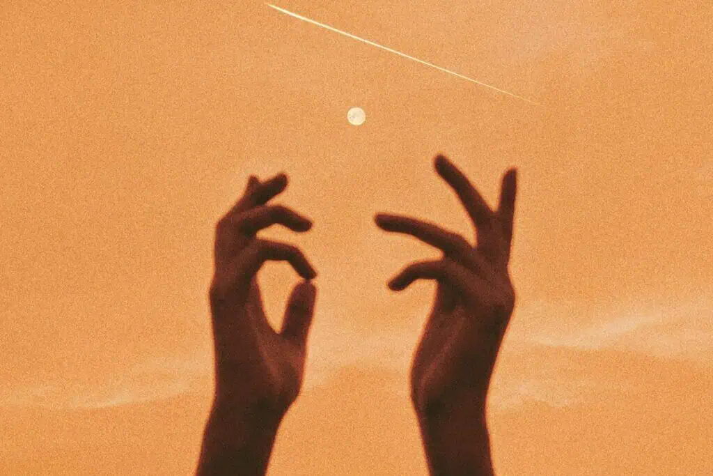 silhouette of hands reaching toward the moon in an orange sky