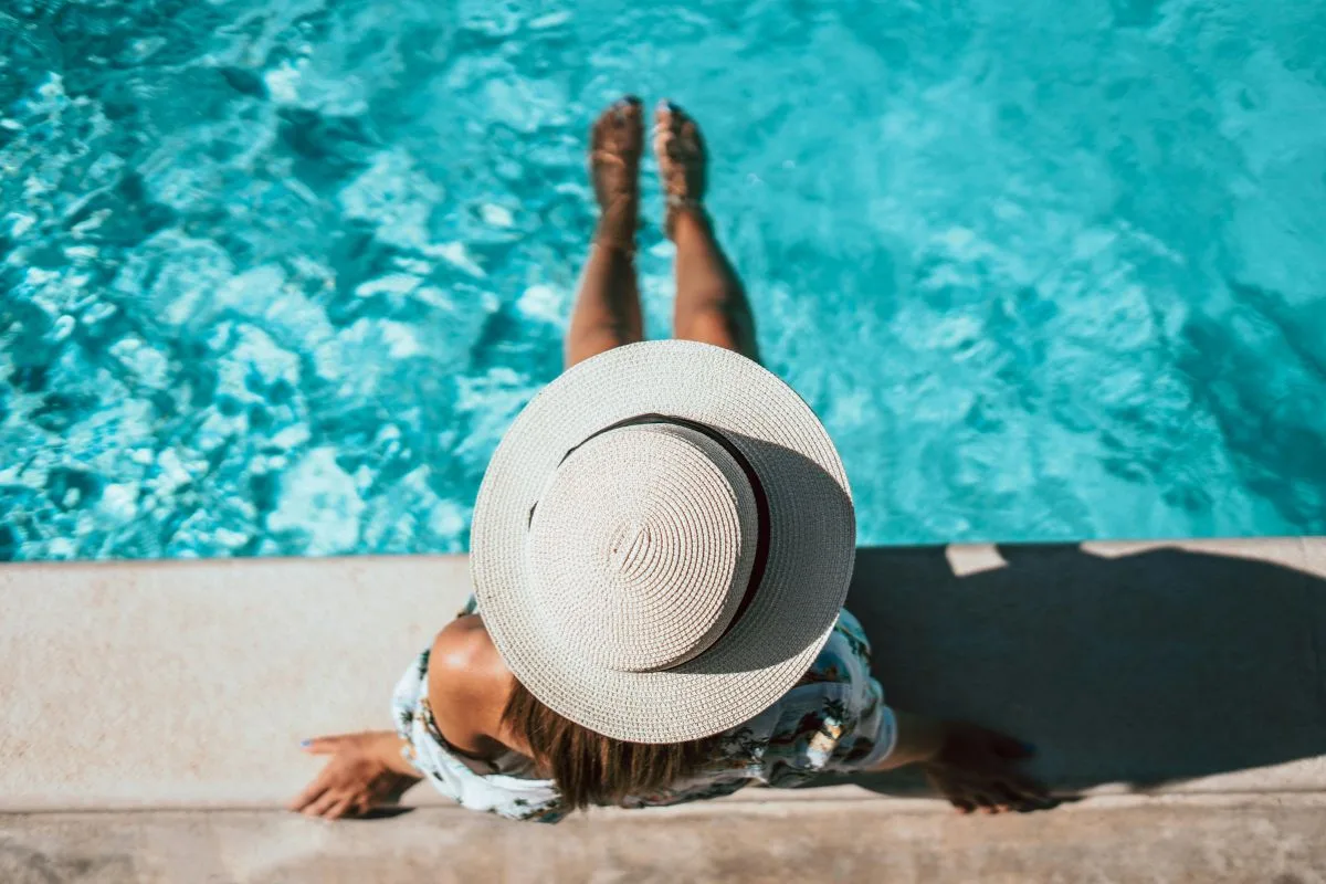 woman in sunhat lounging by a turquoise pool on a sunny summer day