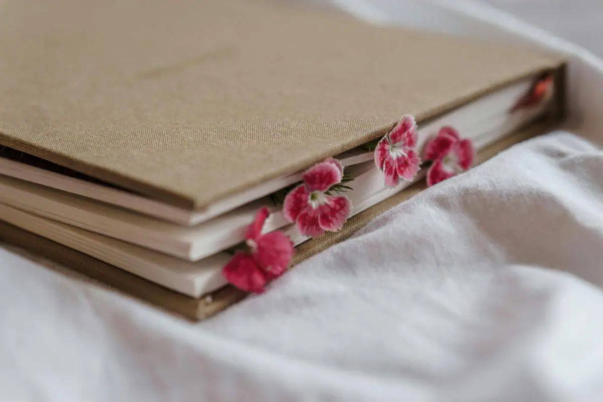 linen-covered journal with pink flowers peeking out between pages on soft white fabric