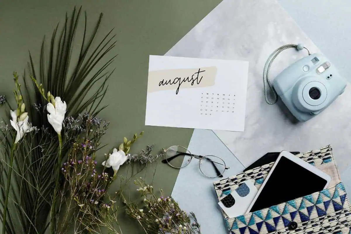 august calendar flatlay with camera, glasses, flowers and tech accessories