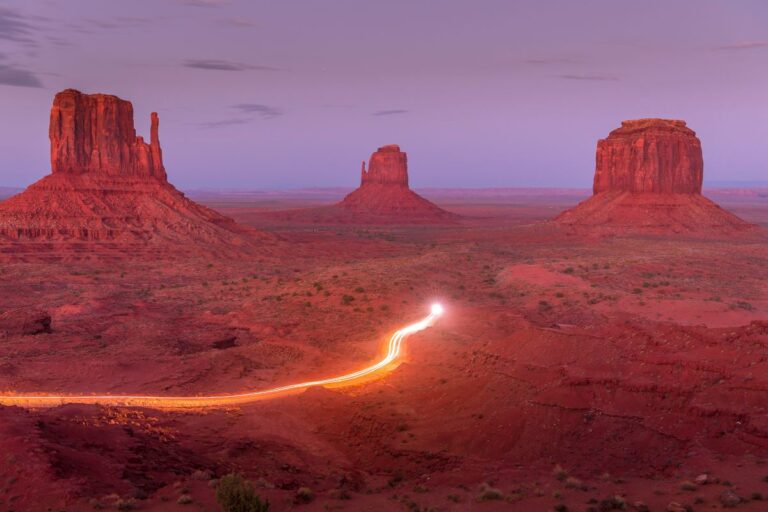 Monument Valley at dusk and the long light trail cutting through the red desert