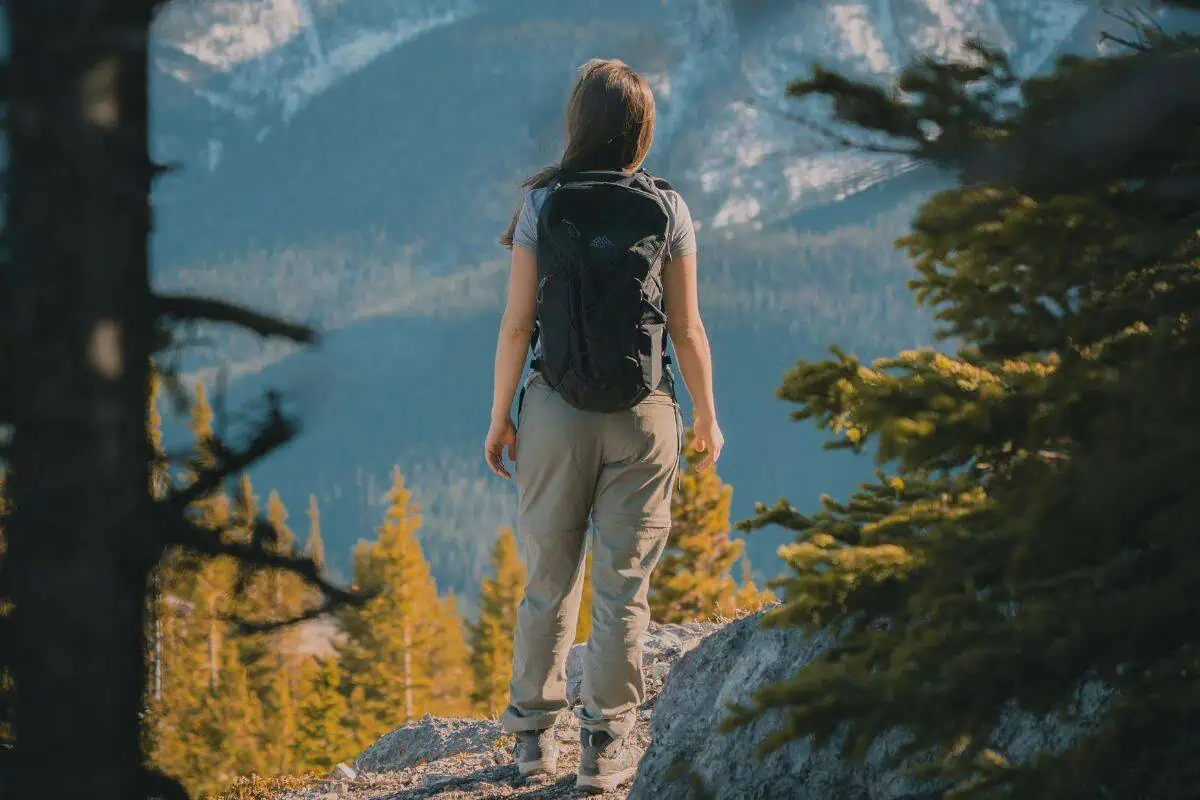 female hiker standing on mountain trail overlooking forested valley