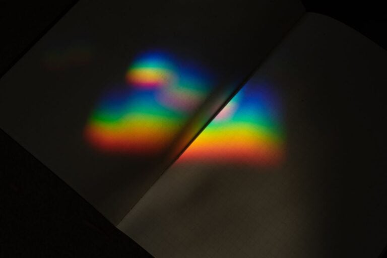 soft rainbow light falling across open book pages in a moody setting, evoking beautiful words and reflection